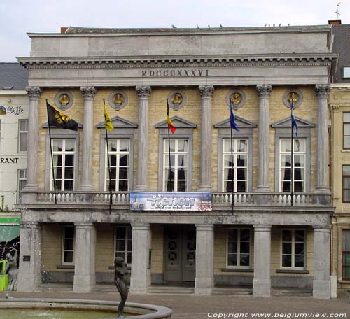 Stadhuis TIENEN foto De massieve voorgevel van de verdieping rust op 6 zware pijlers, verbonden door 5 zware blokken arduin. De bovengevel zit achter 6 Korinthische zuilen. Tussen deze zuilen liggen balkons met een balusterborstwering.