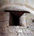 Sint-Pieterskerk KORTESSEM foto: Bij het binnentreden via de poort in de westertoren (toegangsdeur van eind 19de eeuw), zien wij links en rechts twee schietgaten. Deze schietgaten waren de enige in het gelijkvloers van de vestigingstoren die oorspronkelijk los van de kerk stond. 